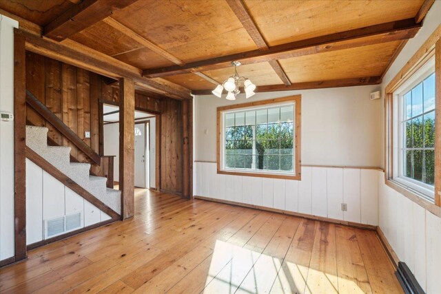 empty room featuring light wood-type flooring, wooden ceiling, a wealth of natural light, and a chandelier