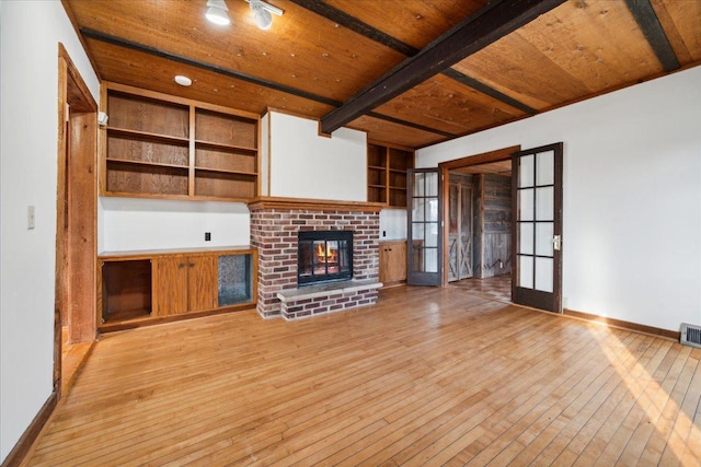 unfurnished living room featuring a fireplace, beamed ceiling, light wood-type flooring, french doors, and wooden ceiling