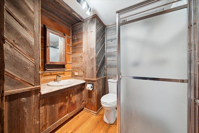 bathroom with toilet, vanity, wooden walls, hardwood / wood-style flooring, and a shower with shower door