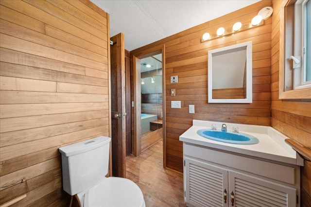 bathroom with a textured ceiling, toilet, vanity, and wood walls