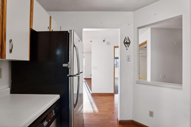 kitchen featuring stainless steel fridge, white cabinetry, light wood-type flooring, and a textured ceiling