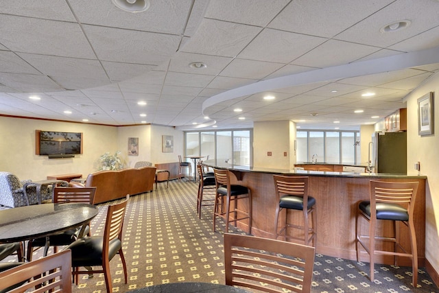 interior space with a drop ceiling, carpet floors, and indoor wet bar