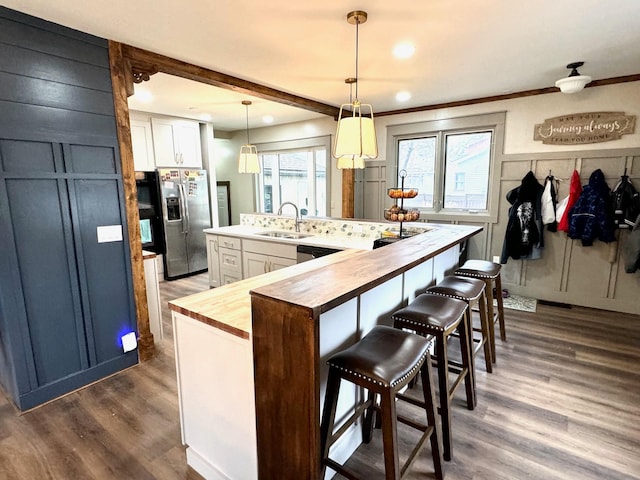 kitchen with white cabinets, sink, an island with sink, decorative light fixtures, and stainless steel fridge