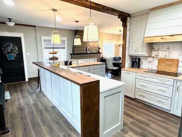 kitchen featuring sink, wooden counters, custom range hood, white cabinets, and pendant lighting