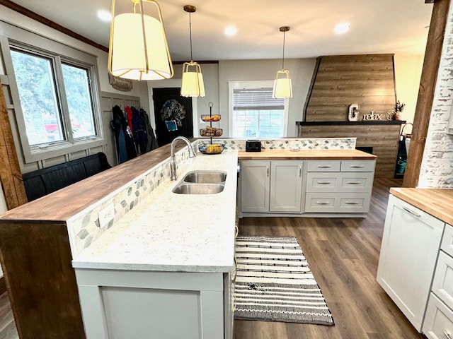 kitchen featuring dark hardwood / wood-style flooring, sink, an island with sink, white cabinetry, and decorative light fixtures