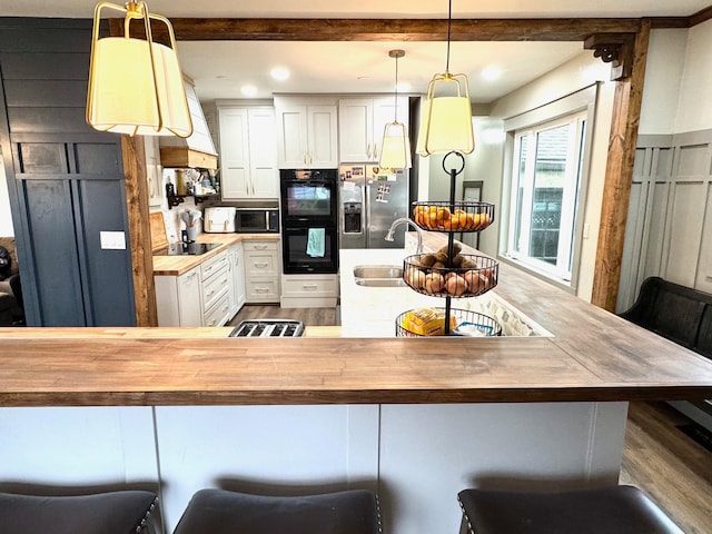 kitchen featuring butcher block counters, pendant lighting, black appliances, and a breakfast bar