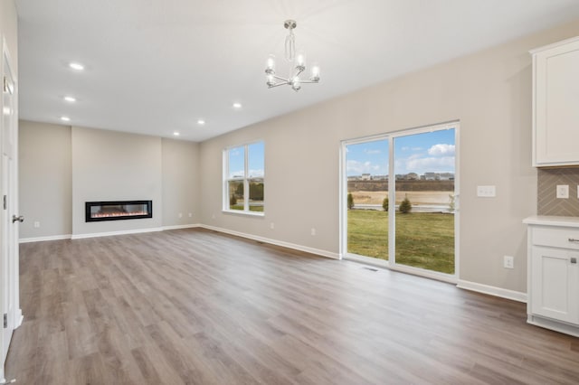 unfurnished living room featuring light wood-type flooring, an inviting chandelier, and a healthy amount of sunlight