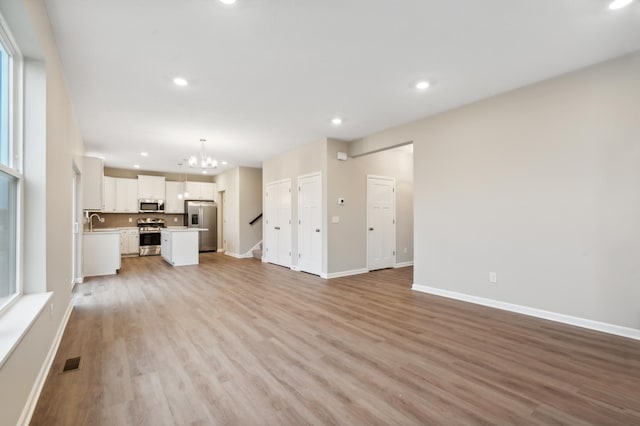 unfurnished living room with light hardwood / wood-style floors, sink, and an inviting chandelier