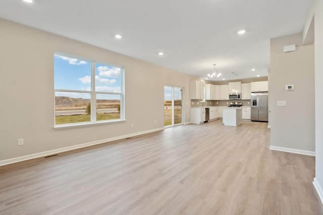 unfurnished living room featuring light wood-type flooring and a notable chandelier