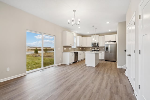 kitchen featuring white cabinets, appliances with stainless steel finishes, a kitchen island, decorative light fixtures, and tasteful backsplash