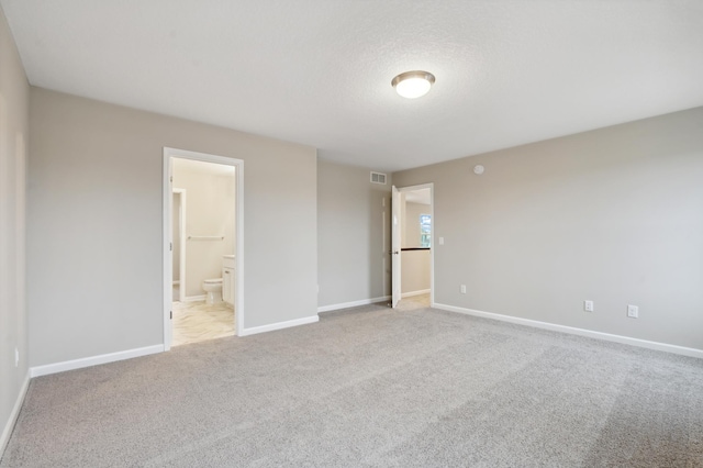 unfurnished bedroom with connected bathroom, light carpet, and a textured ceiling