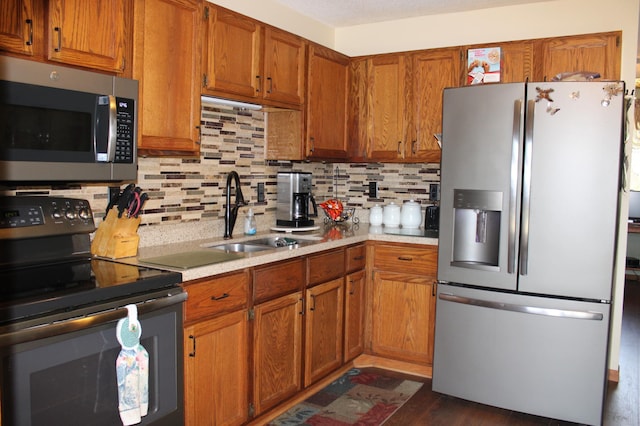 kitchen featuring light countertops, appliances with stainless steel finishes, a sink, and brown cabinets