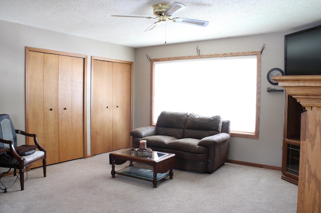 living area with ceiling fan, a textured ceiling, baseboards, and light colored carpet