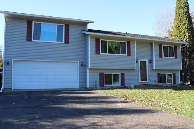 raised ranch featuring a front lawn, driveway, a chimney, and an attached garage