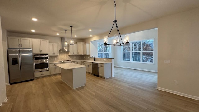 kitchen with appliances with stainless steel finishes, wall chimney exhaust hood, sink, decorative light fixtures, and a kitchen island