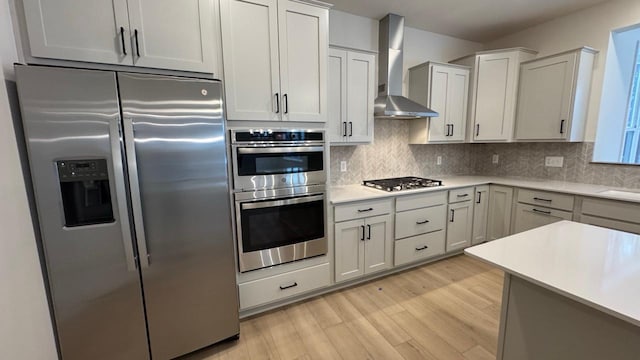 kitchen with sink, light wood-type flooring, tasteful backsplash, wall chimney range hood, and stainless steel appliances