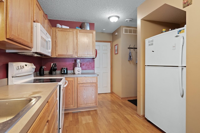 kitchen with light brown cabinets, white appliances, a textured ceiling, and light wood-type flooring