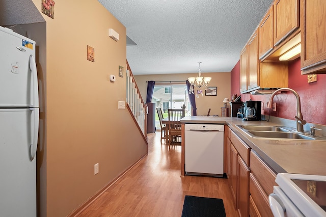 kitchen featuring decorative light fixtures, sink, an inviting chandelier, white appliances, and light hardwood / wood-style flooring