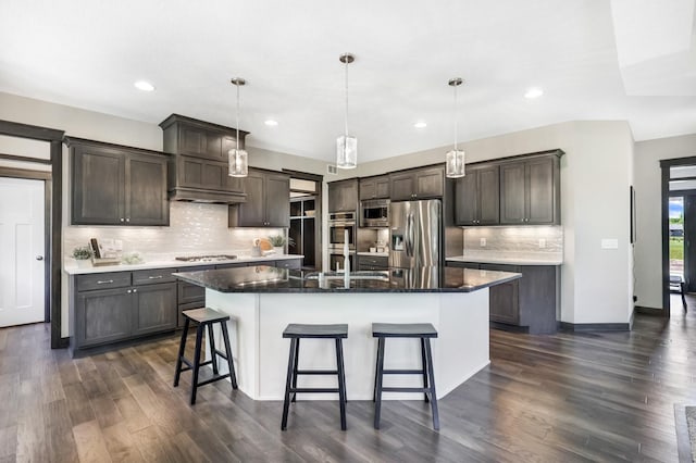 kitchen with dark hardwood / wood-style floors, pendant lighting, dark brown cabinets, a center island with sink, and appliances with stainless steel finishes