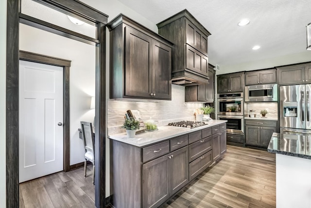 kitchen featuring decorative backsplash, wood-type flooring, dark brown cabinetry, and stainless steel appliances