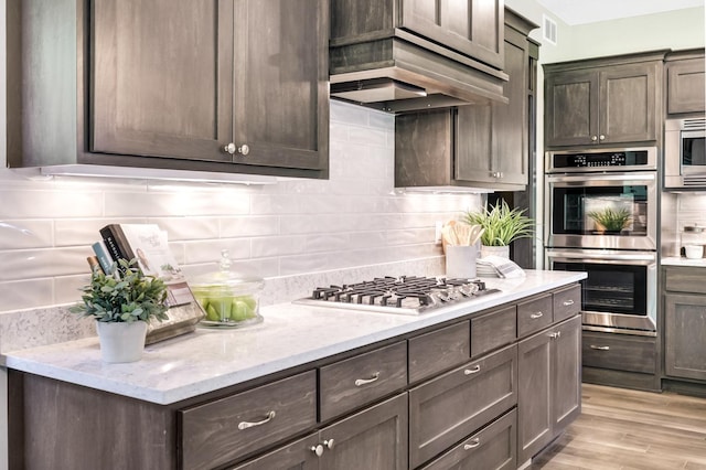 kitchen with dark brown cabinets, light hardwood / wood-style floors, light stone countertops, and appliances with stainless steel finishes