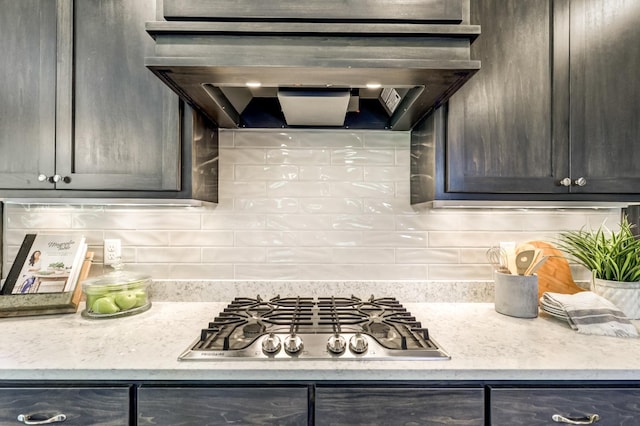 kitchen with tasteful backsplash, light stone counters, exhaust hood, and stainless steel gas stovetop