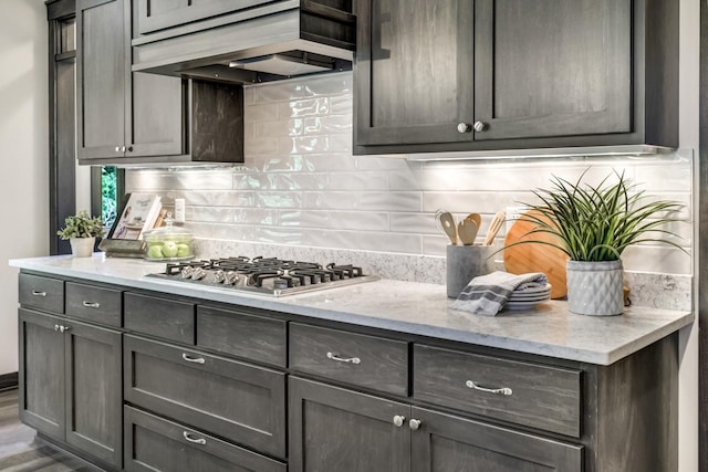 kitchen featuring stainless steel gas stovetop, dark hardwood / wood-style flooring, light stone counters, and backsplash