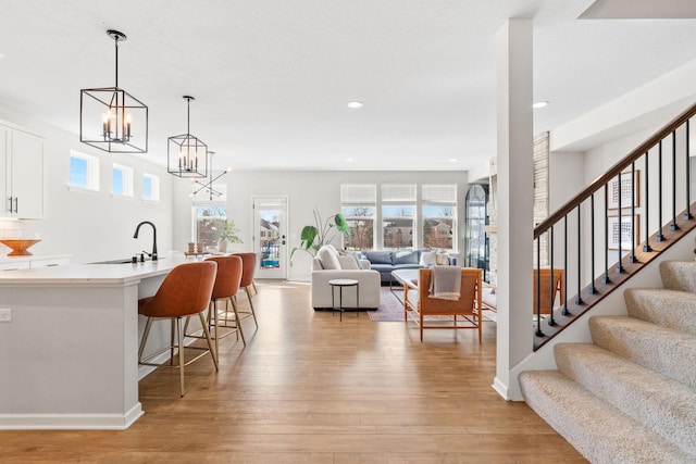 interior space with a kitchen bar, a sink, open floor plan, white cabinets, and light wood finished floors