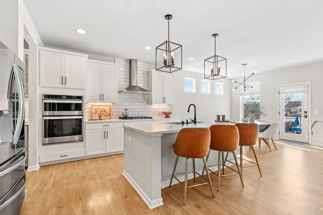 kitchen with tasteful backsplash, light countertops, an inviting chandelier, stainless steel appliances, and wall chimney exhaust hood