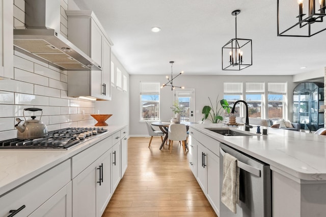 kitchen featuring a sink, light wood-style floors, appliances with stainless steel finishes, wall chimney range hood, and a chandelier