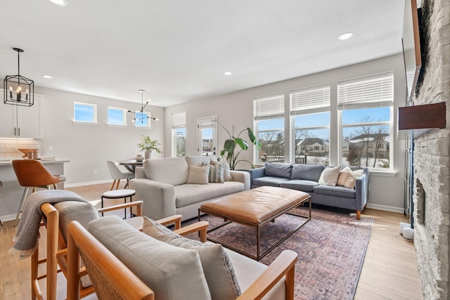 living room with a stone fireplace, an inviting chandelier, light wood-style floors, and baseboards