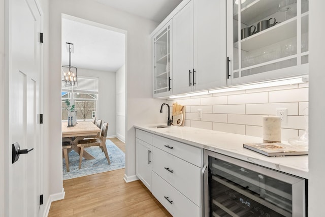 bar with backsplash, beverage cooler, a chandelier, light wood-style flooring, and a sink