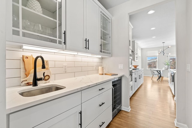 kitchen with a sink, decorative backsplash, wine cooler, glass insert cabinets, and light wood-style floors