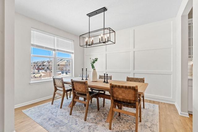 dining room with a decorative wall, baseboards, light wood-type flooring, and a chandelier