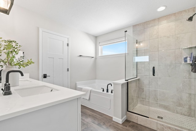 bathroom featuring a sink, a textured ceiling, wood finished floors, a shower stall, and a bath