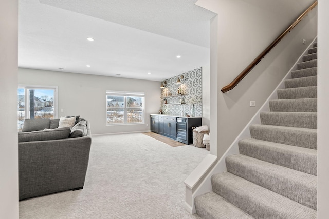 carpeted living area featuring recessed lighting, plenty of natural light, a dry bar, and stairs