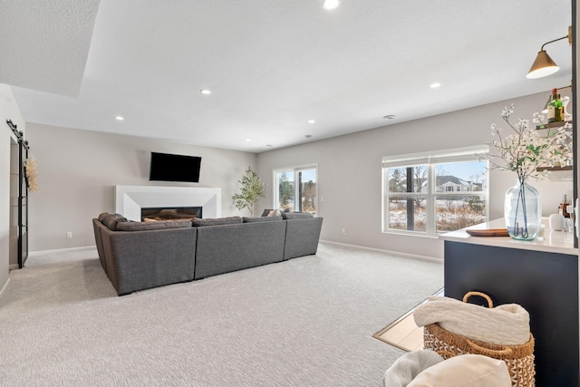 living room featuring a glass covered fireplace, recessed lighting, a barn door, baseboards, and light colored carpet