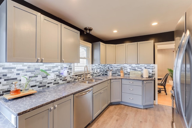 kitchen with sink, light hardwood / wood-style flooring, dark stone counters, decorative backsplash, and appliances with stainless steel finishes