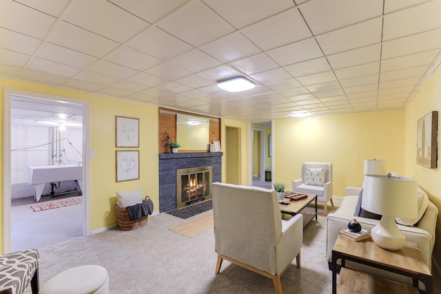 living room featuring carpet flooring, a paneled ceiling, and a brick fireplace