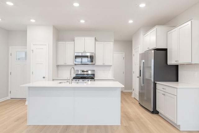 kitchen with a center island with sink, light wood-type flooring, white cabinetry, and appliances with stainless steel finishes