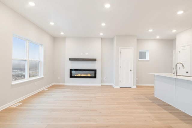 unfurnished living room with light hardwood / wood-style flooring and sink