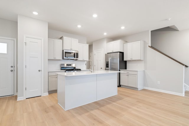 kitchen featuring white cabinetry, stainless steel appliances, decorative backsplash, light hardwood / wood-style flooring, and a kitchen island with sink