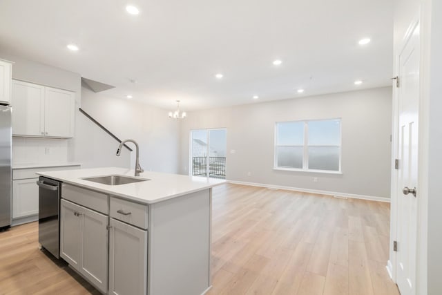 kitchen featuring sink, hanging light fixtures, decorative backsplash, an island with sink, and light hardwood / wood-style floors