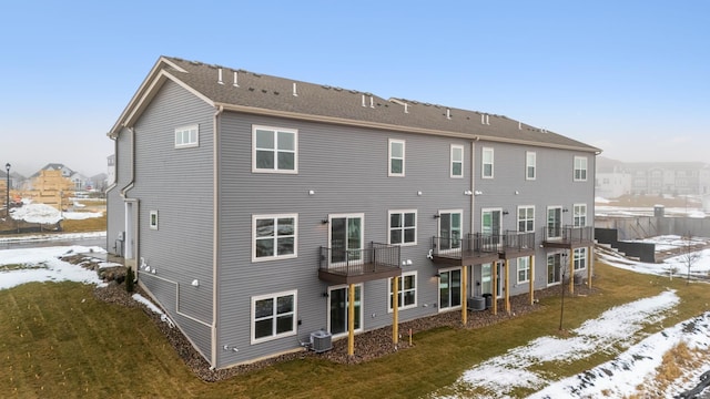 snow covered back of property with cooling unit, a balcony, and a yard