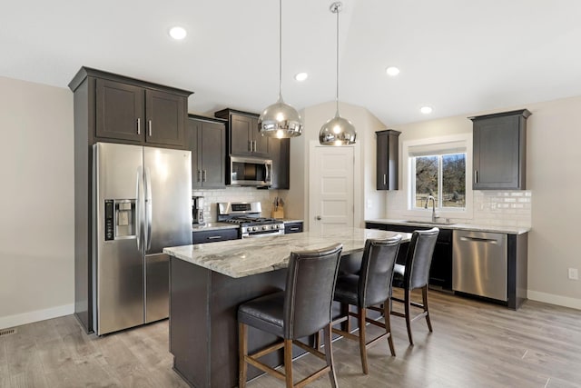 kitchen with stainless steel appliances, a breakfast bar, baseboards, light stone countertops, and light wood finished floors