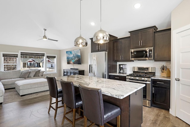 kitchen with light wood finished floors, tasteful backsplash, a breakfast bar area, stainless steel appliances, and dark brown cabinets