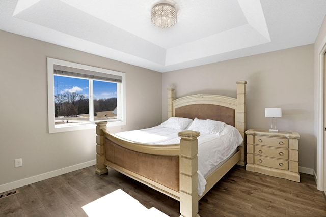 bedroom featuring dark wood-style flooring, a raised ceiling, and baseboards