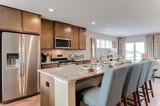 kitchen featuring a kitchen bar, a center island with sink, light hardwood / wood-style flooring, and appliances with stainless steel finishes