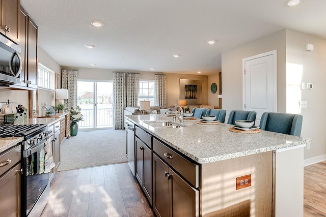 kitchen with light stone counters, stainless steel appliances, light wood-type flooring, sink, and an island with sink