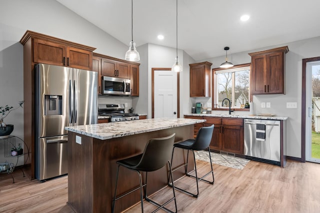 kitchen with light wood finished floors, a sink, vaulted ceiling, appliances with stainless steel finishes, and a center island